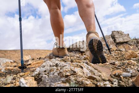 Close-up of hiker's legs with trekking poles walking on rocky trail Stock Photo