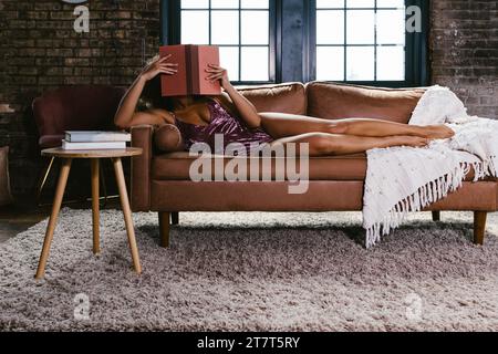 Mixed race female dancer in pink leotard on couch reading a book Stock Photo