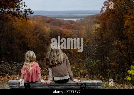 Two people sitting on bench looking at view of fall foliage Stock Photo