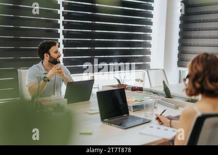 Happy, smiley, male business person having a conversation with his colleagues while working on lap top. Stock Photo