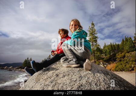Boy smiling at camera while sitting next to brother on top of boulder Stock Photo