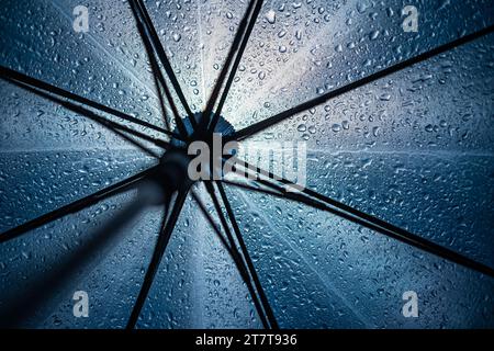 Raindrops on open umbrella seen from below against city lights at night. Selective focus, colored bokeh balls, no people. Stock Photo