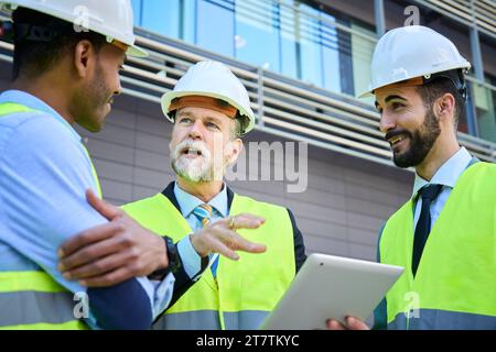 Several concentrates engineers talk carefree outdoor. Meeting three smiling multiracial architects. Stock Photo