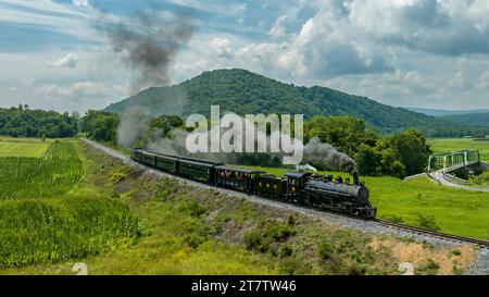 Rockhill Furnace, Pennsylvania, August 5, 2023 - An Aerial View of a Steam Narrow Gauge Passenger Train Approaching Runk Rd. Bridge on a Sunny Summer Stock Photo