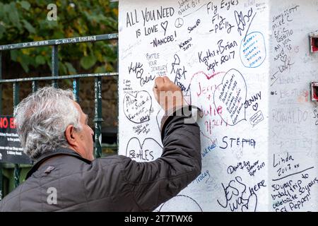 A man writes a message amongst many similar messages on a section of the wall outside Abbey Road Studios in London, UK, famously used by the Beatles Stock Photo