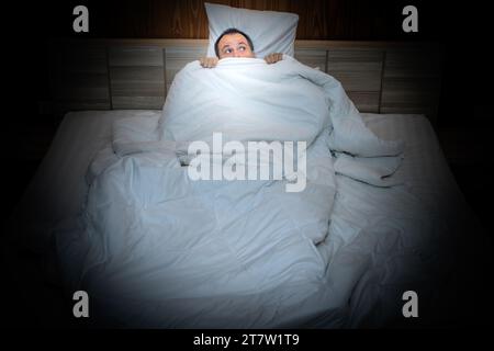 Frightened man in bed hiding under the covers Stock Photo