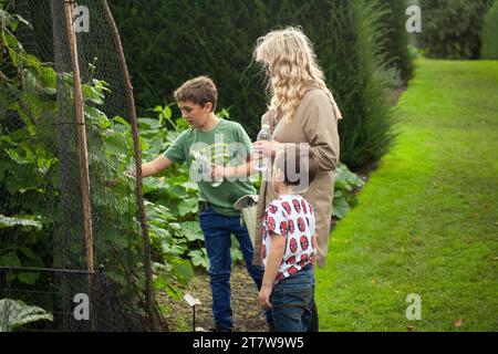 A mother and her two children share a stroll through a country garden and vegetable patch. Inquisitive, the young boy asks mother about the vegetables Stock Photo