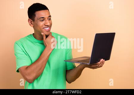 Photo portrait of nice young male touch chin working minded netbook dressed stylish green outfit isolated on beige color background Stock Photo