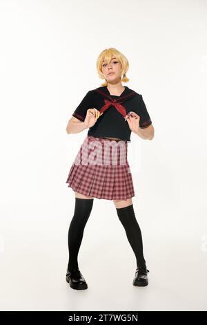 confident anime style woman in plaid skirt touching red neckerchief and looking at camera on white Stock Photo