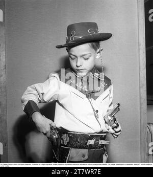 Boy in the 1950s. A boy is dressed in cowboy clothes, shirt, gun holster and cowboy hat and holds two toy revolvers. 1950. Kristoffersson ref AZ47-7 Stock Photo