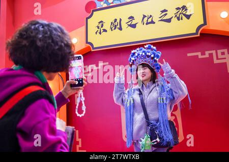 (231117) -- KUNMING, Nov. 17, 2023 (Xinhua) -- A visitor poses for a photo with headwear of Peking Opera at the exhibition zone of Beijing during the China International Travel Mart 2023 in Kunming, southwest China's Yunnan Province, Nov. 17, 2023. The China International Travel Mart 2023 kicked off Friday in Kunming. Themed 'Nihao! China,' the three-day event is co-sponsored by China's Ministry of Culture and Tourism, the Civil Aviation Administration of China and the provincial government of Yunnan. The fair, with an exhibition area of some 90,000 square meters, features six special exh Stock Photo