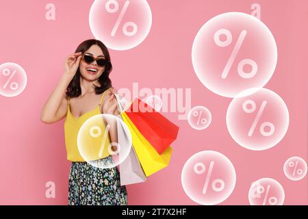 Discount offer. Happy woman with paper shopping bags on pink background. Bubbles with percent signs flying near her Stock Photo