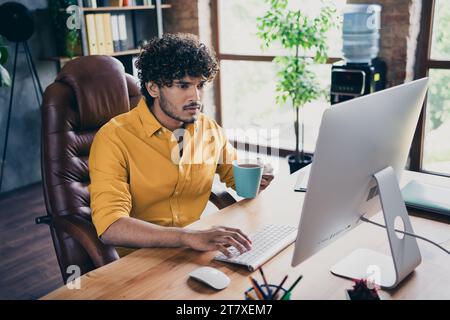 Photo portrait of handsome young guy wear yellow shirt focused busy manager coffee mug workplace stylish room interior home office design Stock Photo