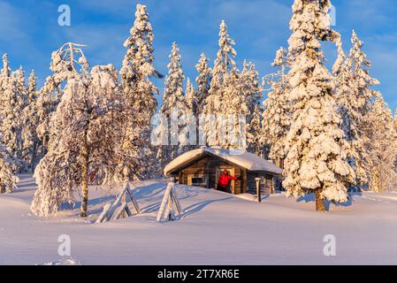 Tourist in the early morning sun stands in front of an isolated chalet in the snowy forest, Norrbotten, Swedish Lapland, Sweden, Scandinavia, Europe Stock Photo