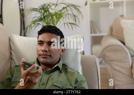 Happy biracial man lying on sofa using smartphone at home Stock Photo