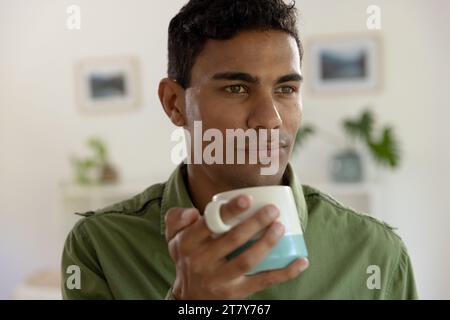 Thoughtful biracial man holding mug and looking away at home Stock Photo