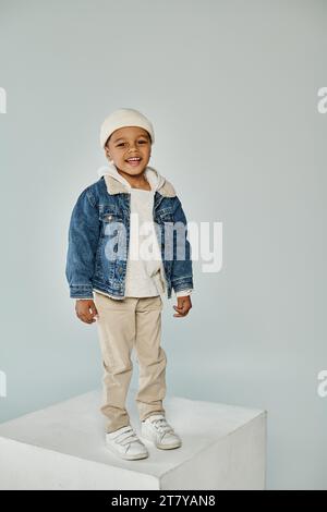 cheerful african american preschooler boy in winter attire and beanie hat on grey backdrop Stock Photo