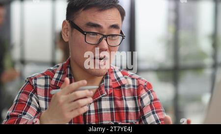 Portrait of a successful Asian software engineer working on a laptop at his desk. Stock Photo