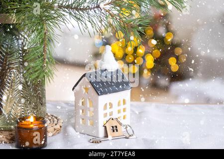 Key and tiny house of a small size on cozy home with Christmas decor on table of festive kitchen. Gift for New Year. Insurance, moving to new house, m Stock Photo