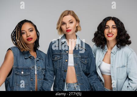three attractive multiracial women in denim clothes looking at camera on grey, group portrait Stock Photo