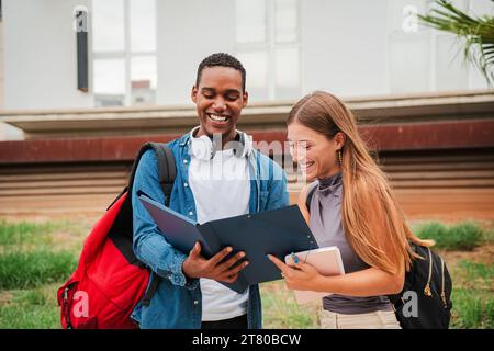 High school student guy smiling while showing his female colleague the homeworks and the lesson for the exam. Two multiracial friends reading, checking results of a test, talking at university campus. High quality photo Stock Photo