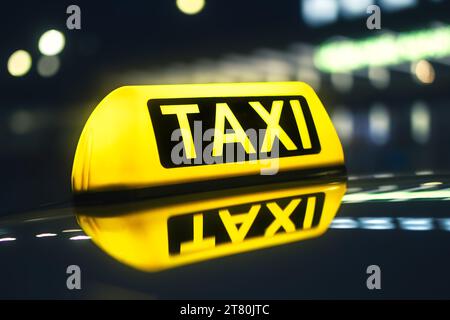 Selective focus on yellow taxi sign. Reflection in roof of car against neon lights of city street at night. Stock Photo