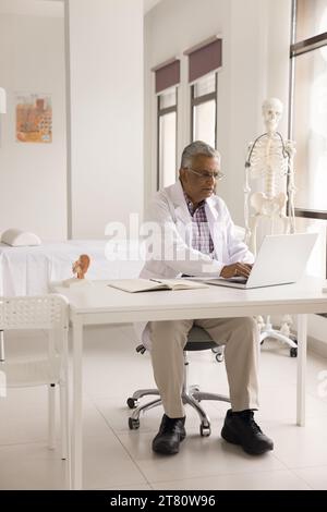 Serious elderly Indian practitioner man working at laptop Stock Photo
