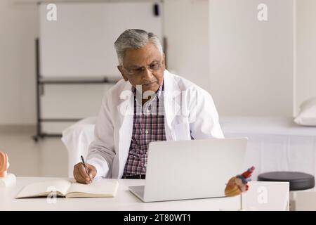 Focused senior Indian doctor making records in medical history book Stock Photo