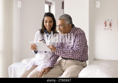 Excited old Indian patient and happy young doctor using tablet Stock Photo