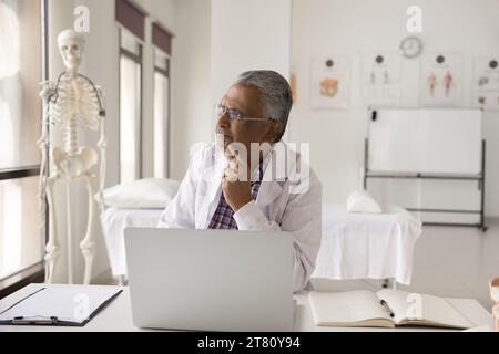 Serious thoughtful senior Indian doctor thinking on job tasks Stock Photo