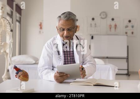 Serious mature Indian doctor using medical application on tablet Stock Photo