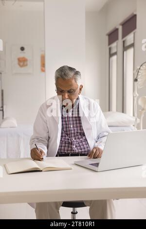 Serious focused older Indian practitioner man writing medical notes Stock Photo