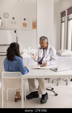 Serious mature Indian physician man meeting with patient in clinic Stock Photo