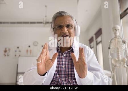 Serious caring practitioner in wireless headphones talking on video call Stock Photo