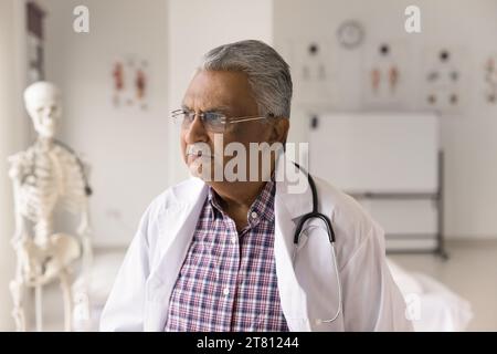 Serious pensive grey haired Indian doctor man looking away Stock Photo