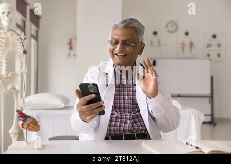 Cheerful senior Indian doctor man giving online consultation on smartphone Stock Photo