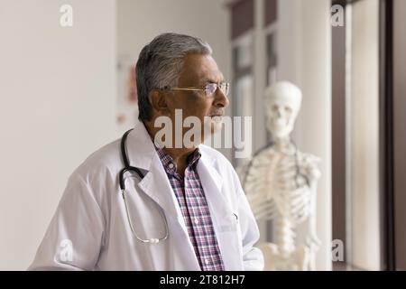 Serious elder Indian doctor man looking at window away Stock Photo