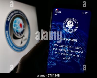 Person holding cellphone with webpage of Direction Generale de la Securite Exterieure (DGSE) in front of logo. Focus on center of phone display. Stock Photo