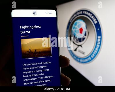 Person holding smartphone with web page of Direction Generale de la Securite Exterieure (DGSE) in front of logo. Focus on center of phone display. Stock Photo