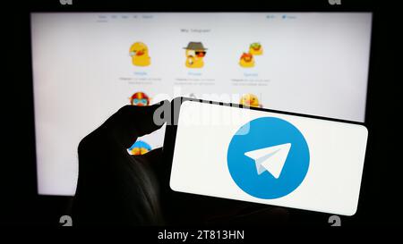 Person holding cellphone with logo of instant messaging service Telegram Messenger in front of webpage. Focus on phone display. Stock Photo