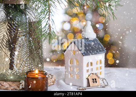 Key and tiny house of a small size on cozy home with Christmas decor on table of festive kitchen. Gift for New Year. Insurance, moving to new house, m Stock Photo