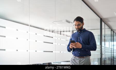 Busy Indian business man project manager holding smartphone walking in office. Stock Photo