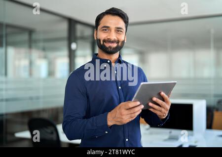 Smiling Indian businessman using tab computer working standing in office. Stock Photo