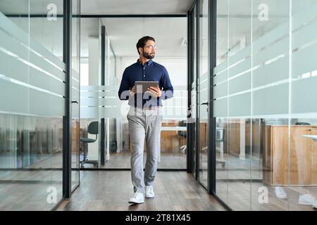 Confident Indian business man looking aside walking with tablet in office. Stock Photo