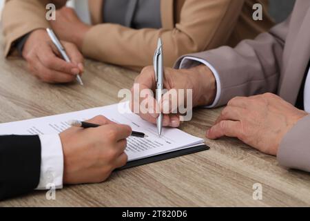Manager showing client where he must to mark signature at light wooden table indoors, closeup Stock Photo