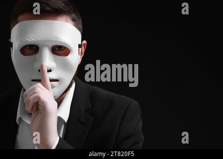 Man in mask and gloves showing hush gesture against black background. Space for text Stock Photo