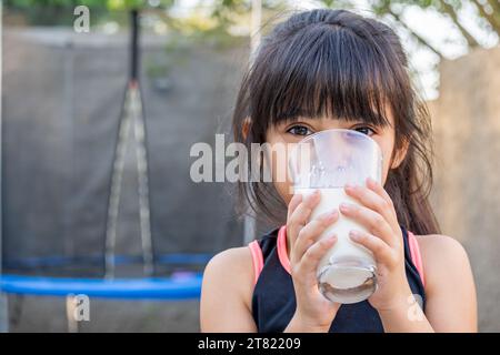 Close-up portrait of her. She drinks a glass of cold milk after playing outside her house. Stock Photo