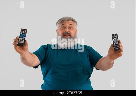 Mature man with TV remote controls on light background Stock Photo