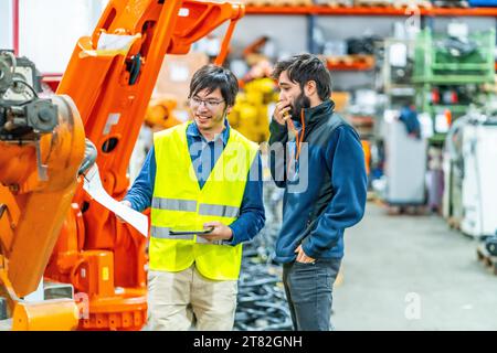 Software engineer explaining to controlling robotic welding process to welder in factory Stock Photo