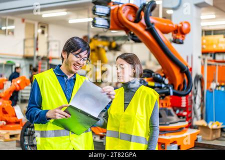 Male and female multi-ethnic engineers reading data while working in a robotic industry Stock Photo